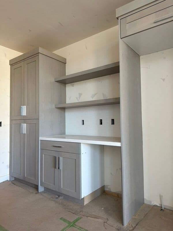 Modern gray kitchen cabinetry with open shelves and a workspace area, under construction.
