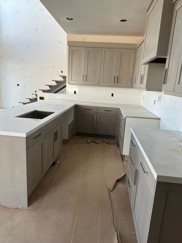 Modern kitchen with gray cabinets, white countertops, and unfinished walls under construction.