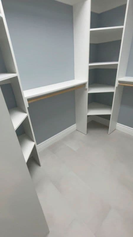 Empty modern closet with white shelves and gray walls, featuring a light floor.