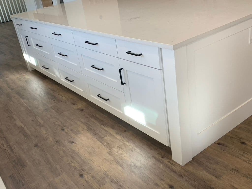 Modern kitchen island with white cabinetry and black handles on light wood floor.