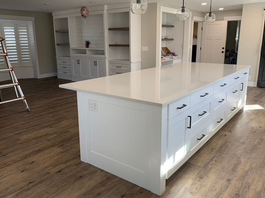 Modern kitchen with white island, drawers, and wooden flooring, featuring open shelving.