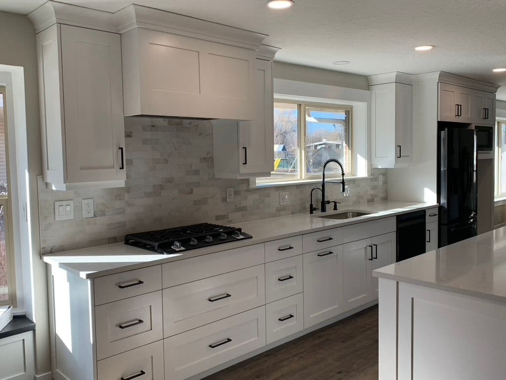 Modern kitchen with white cabinets, black fixtures, and marble backsplash, featuring a gas stove.
