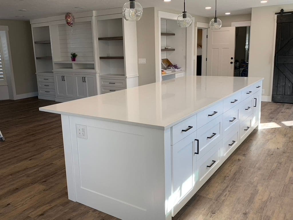 Modern kitchen with white island, black hardware, and open shelving in bright, airy space.