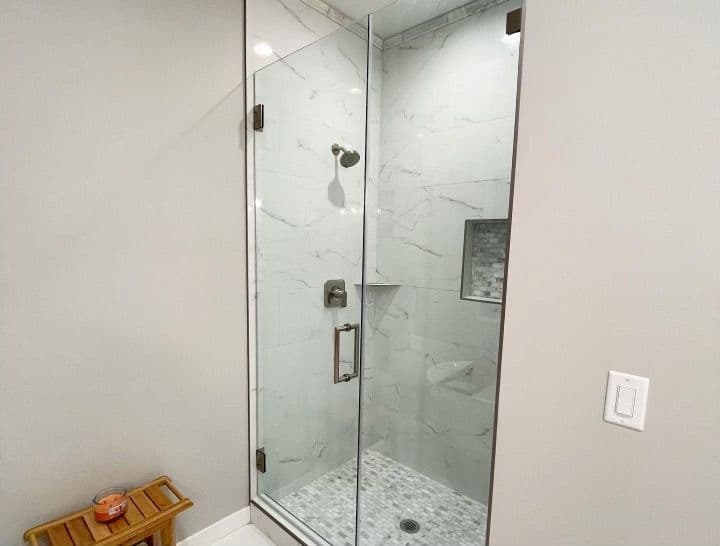 Modern glass shower featuring marble walls and pebble floor, complemented by wooden bench.