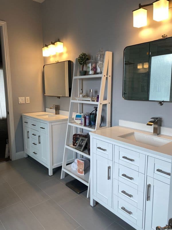 Modern bathroom with dual sinks, white cabinets, a ladder shelf, and stylish lighting.