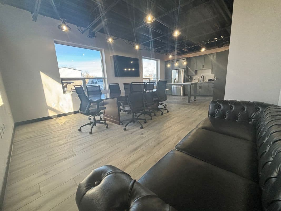 Modern office interior featuring a conference table, ergonomic chairs, and a leather couch.