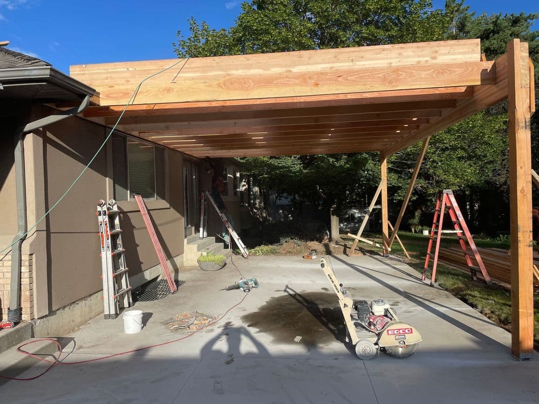 Wooden pergola construction at a home, featuring tools and scaffolding on a concrete slab.
