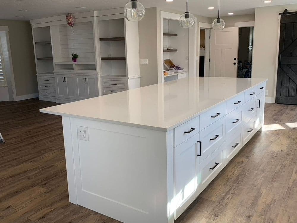 Modern kitchen featuring a large white island with drawers, open shelving, and wood flooring.