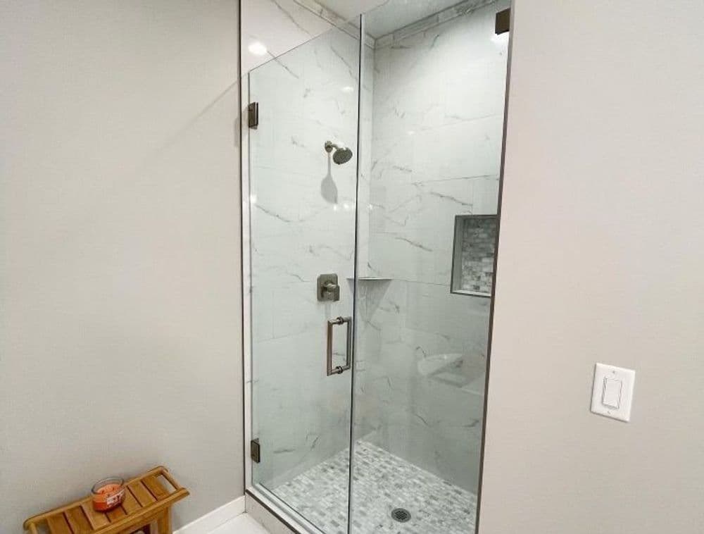 Modern glass shower enclosure with marble walls and pebble stone flooring, styled for elegance.