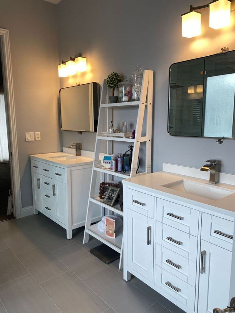 Modern bathroom with double sinks, stylish mirror, and ladder shelf for storage. Bright lighting.